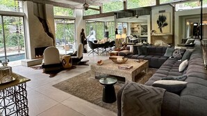 Un salon spacieux avec un grand canapé gris, une table basse en pierre et une cheminée. Une grande fenêtre offre une vue sur l’extérieur.