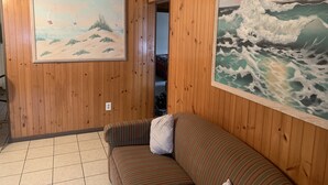 Une pièce aux murs lambrissés, avec un canapé à rayures et deux grands tableaux représentant des paysages et des vagues.
