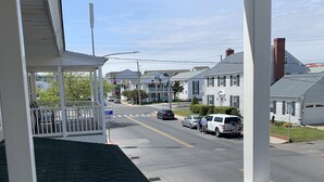 Une véranda couverte donnant sur une rue, des maisons et des voitures garées.