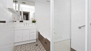 Une salle de bain moderne avec des carreaux blancs, un meuble-lavabo blanc avec un miroir, une baignoire et un espace douche.