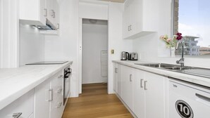 A modern kitchen with white cabinets, a wooden floor, a stainless steel sink, and a window with a view of buildings.