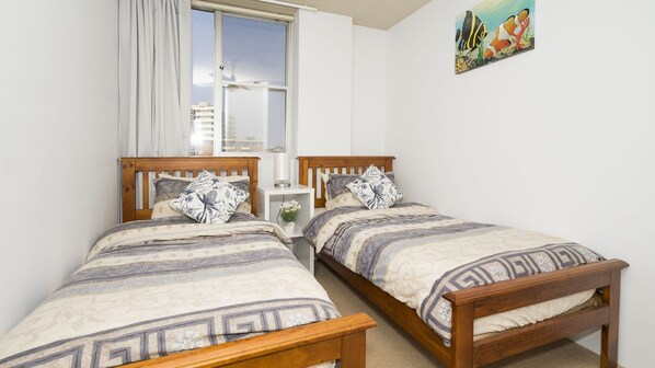 A bedroom with two wooden beds, a nightstand, a window with curtains, and a wall-mounted painting.
