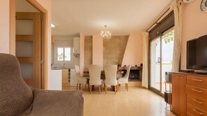 A cozy living room with a sofa, a dining area with chairs, a fireplace, and a TV. - Apartment Regina by Interhome (Torredembarra)