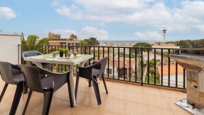 A balcony with a table and chairs, a grill, and a view of the sea and buildings. - Apartment Regina by Interhome (Torredembarra)