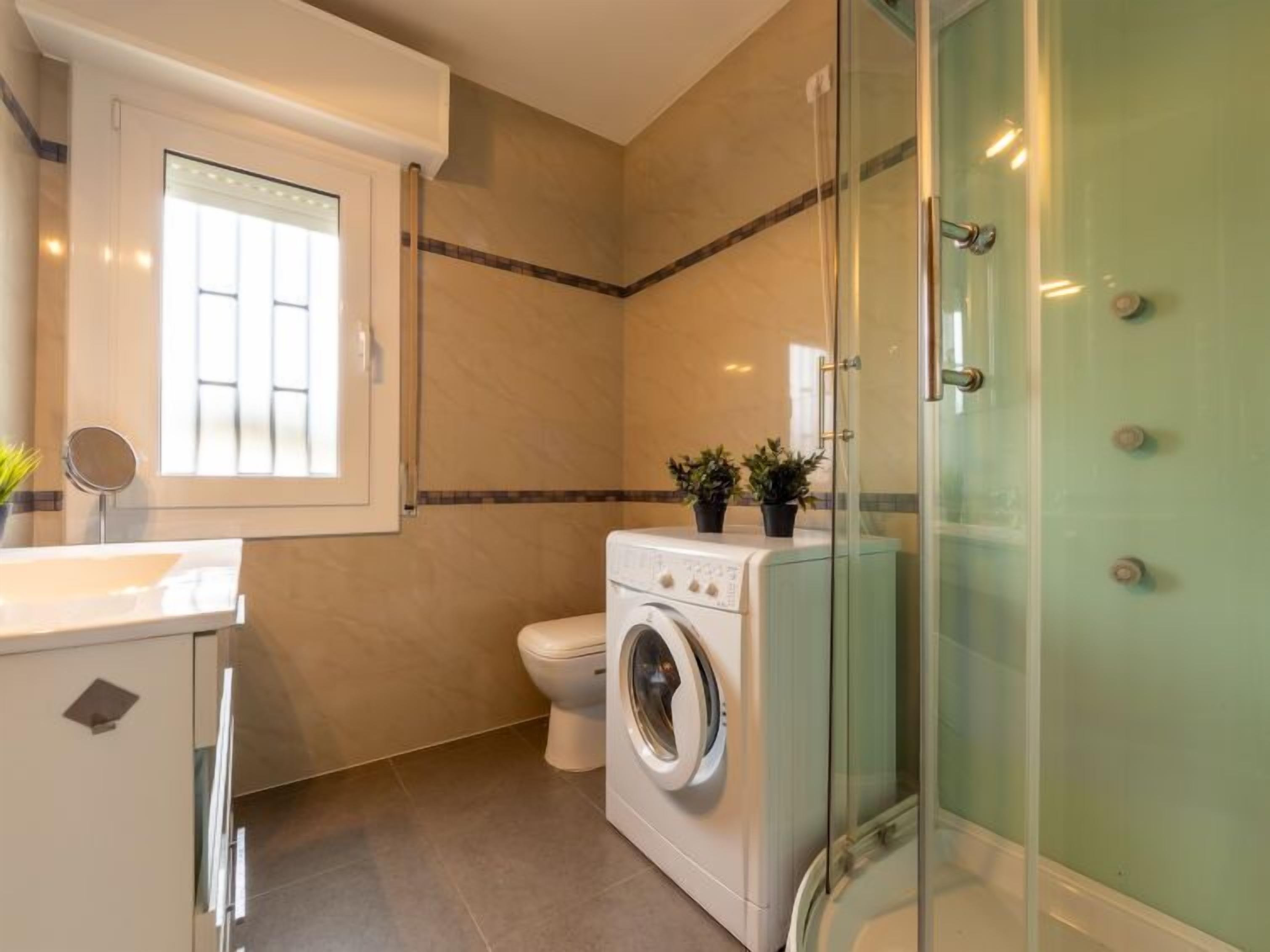 A compact bathroom with a washing machine, toilet, and a glass shower enclosure.