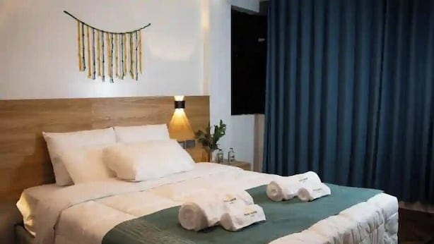 A neatly made bed with white linens, a green throw blanket, and two rolled towels on the bed. - Marvelous Plaza (Cusco)