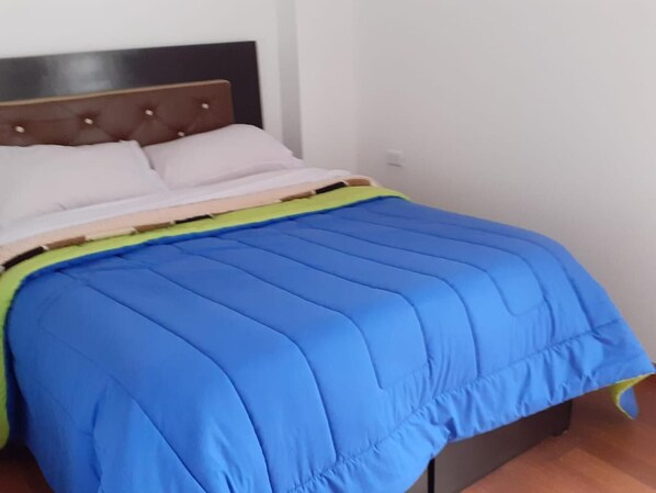 A bed with a blue quilt, a green blanket, and two white pillows.