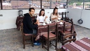 A dining area with a table set for three people, wooden chairs, and a view of the city through large windows. - Marvelous Plaza (Cusco)