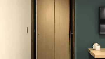 Un pasillo con una puerta de madera, una mesita con un abanico de papel y un televisor montado en una pared azul verdoso.