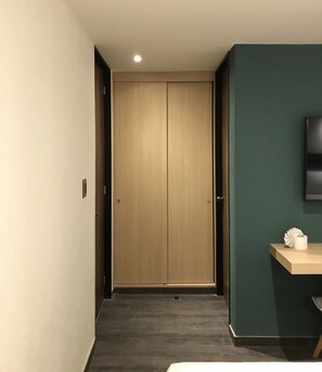 Un couloir avec une porte en bois, une petite table sur laquelle repose un éventail en papier, et un téléviseur fixé au mur, lequel est peint dans une teinte turquoise.
