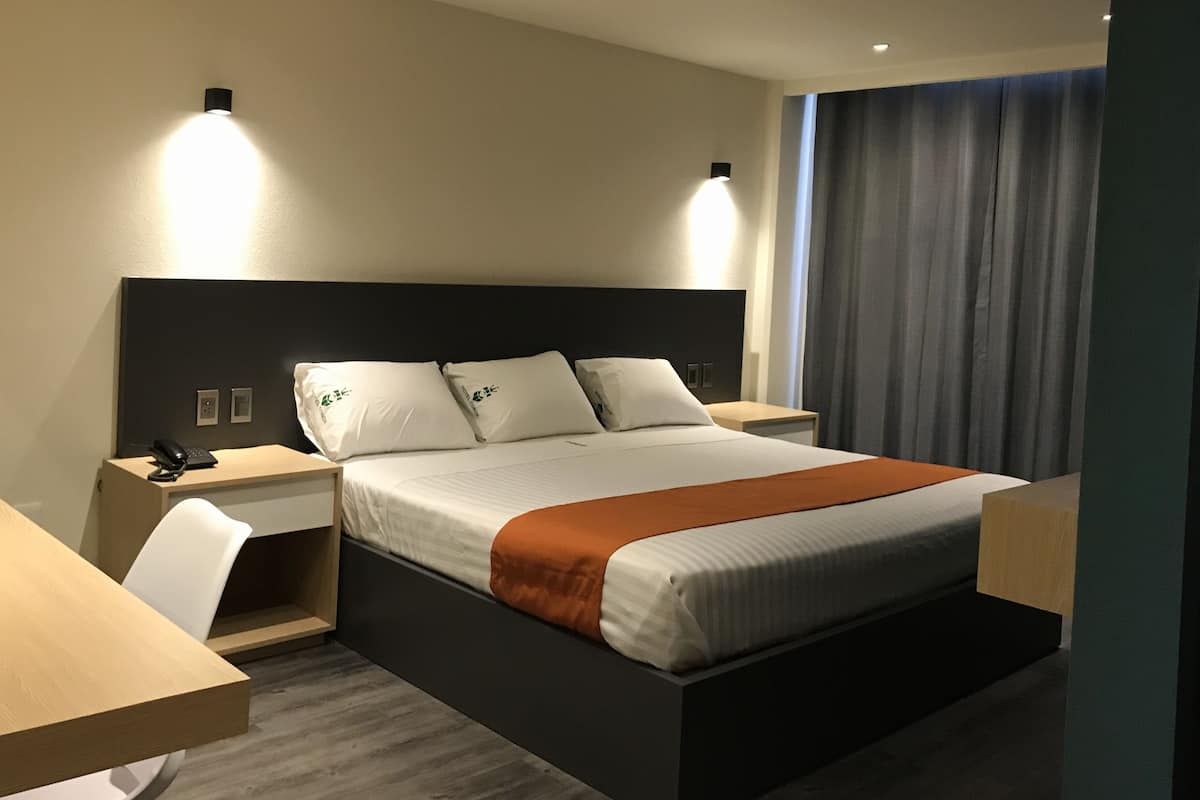 A modern hotel room with a large bed, bedside tables, a desk, and a chair.