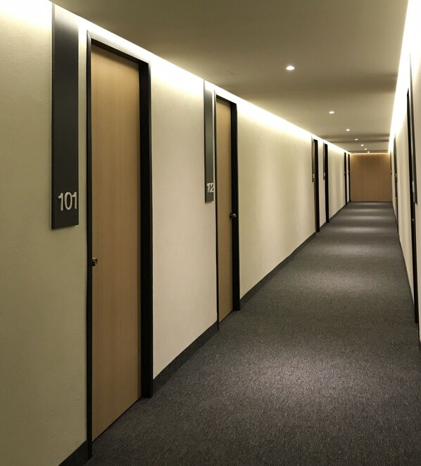Corredor com portas numeradas 101 e 102, piso coberto de carpete e iluminação embutida.