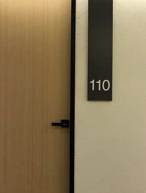 Une porte en bois avec une poignée noire et une plaque noire fixée au mur, portant le numéro 110.