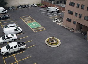 Un estacionamiento con espacios demarcados, una fuente y un edificio de fachada uniforme.