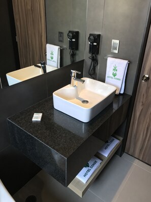 Une salle de bain moderne avec deux lavabos, un miroir et un porte-serviettes orné du logo d’un hôtel.