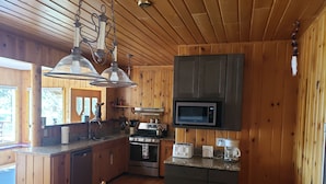 Une cuisine rustique aménagée dans une cabane en bois, avec une table à manger, des placards en bois, un four à micro-ondes, une cuisinière et un évier.