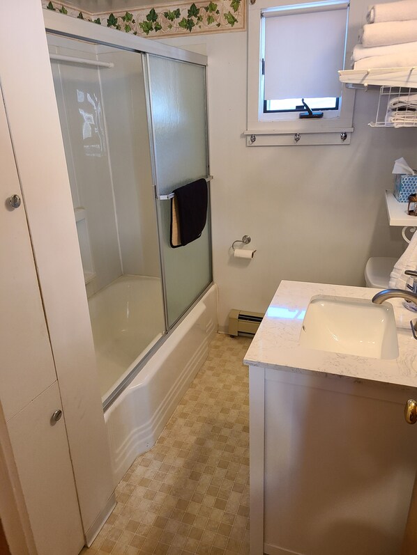 A bathroom with a glass-enclosed shower, a white sink, and a small window above the mirror.