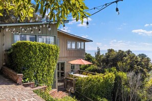 A two-story house with a patio, a view of the ocean, and string lights.