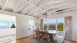 A dining area with a wooden table and chairs, a chandelier, and large windows with a view. - Charming Cottage with Beautiful Ocean Views (Laguna Beach)