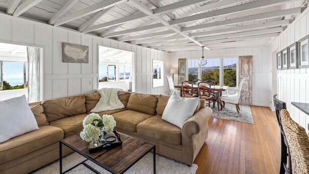A spacious living room with a large beige sectional sofa, a wooden coffee table, and a dining area with a table and chairs. - Charming Cottage with Beautiful Ocean Views (Laguna Beach)