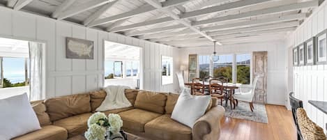 A spacious living room with a large beige sectional sofa, a wooden coffee table, and a dining area with a table and chairs.