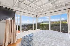A bedroom with a large bed, a television, and multiple windows offering a view of the landscape.