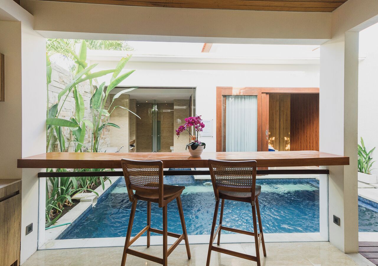 Un bar junto a la piscina con dos sillas de madera, una orquídea en maceta y vistas a una piscina y vegetación.