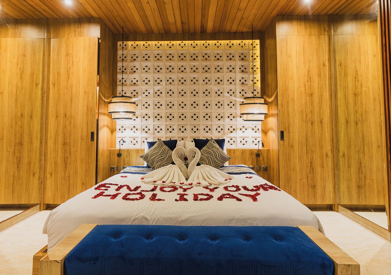 A hotel room with a wooden ceiling, a bed with a white and red bedspread, and a blue upholstered bench.