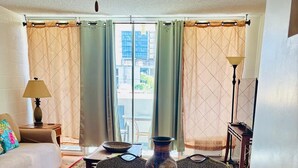 A living room with a sofa, a coffee table, a decorative vase, and a view of buildings through the window. - ~Waikiki~ LOWEST RATES IN AREA ~ 2 Bedroom ~ Fully Furn ~ Blocks to Beach ~ (Honolulu)