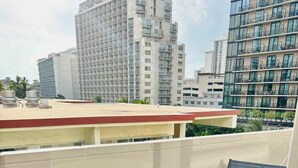 A balcony with a glass table and two chairs, overlooking a cityscape with modern buildings. - ~Waikiki~ LOWEST RATES IN AREA ~ 2 Bedroom ~ Fully Furn ~ Blocks to Beach ~ (Honolulu)