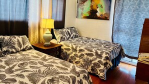 A hotel room with two beds, a ceiling fan, a painting on the wall, and a window with curtains. - ~Waikiki~ LOWEST RATES IN AREA ~ 2 Bedroom ~ Fully Furn ~ Blocks to Beach ~ (Honolulu)