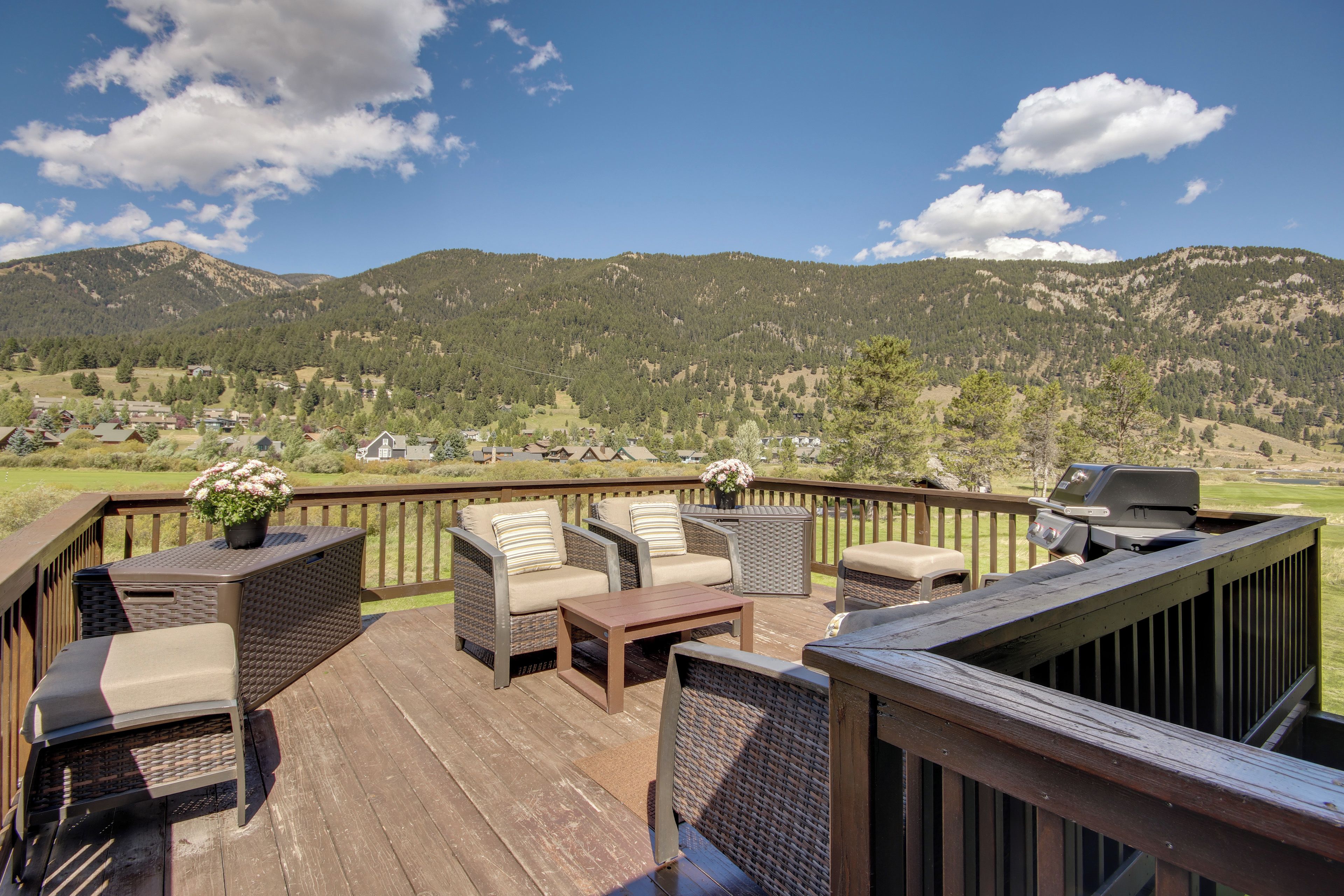 Une terrasse dotée de meubles en osier et d’un barbecue, offrant une vue sur un paysage montagneux.