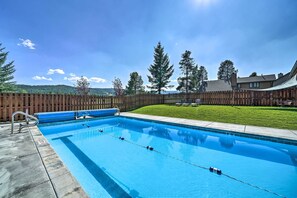Una piscina rectangular amb una tanca de fusta i una zona enjardinada al fons.