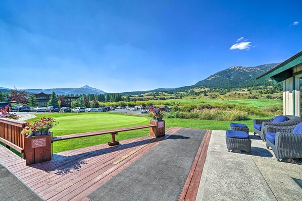 Une terrasse dotée de meubles en osier, offrant une vue sur un terrain de golf et des montagnes.