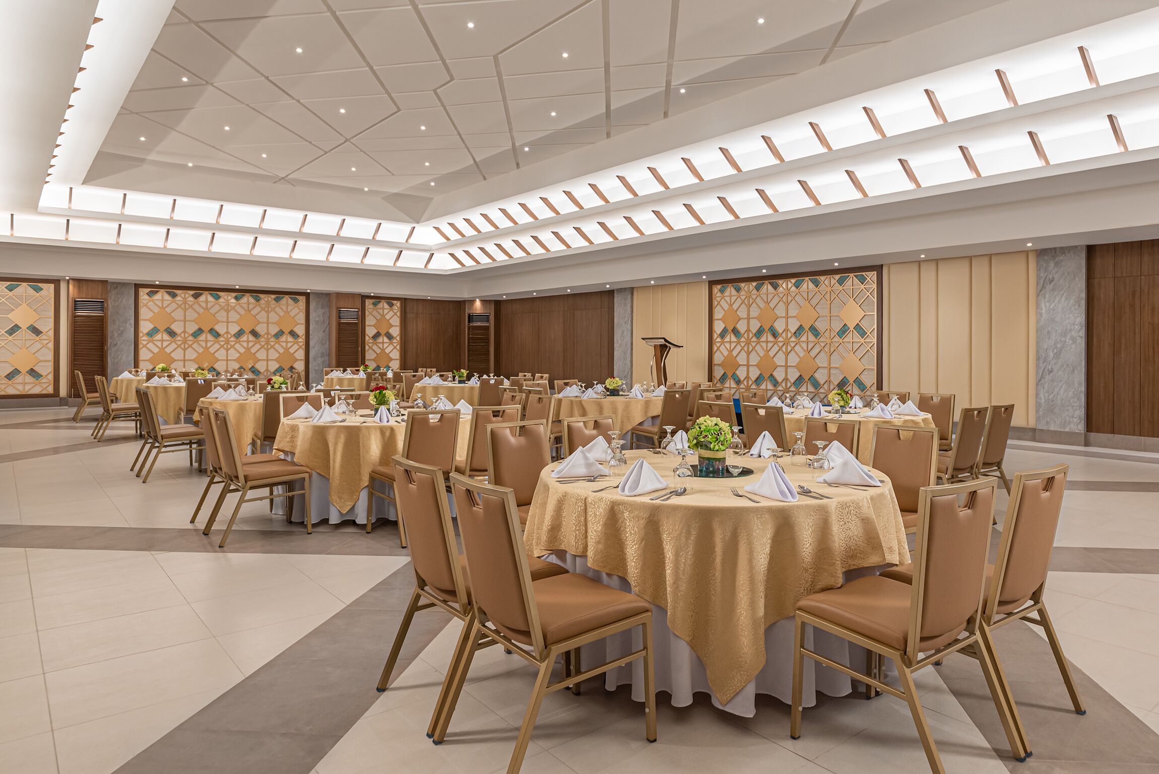 A large banquet hall with round tables covered in gold tablecloths, arranged in rows with chairs.
