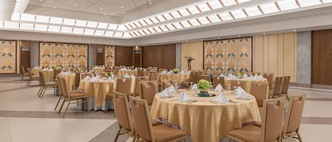 A large banquet hall with round tables covered in gold tablecloths, arranged in rows with chairs.