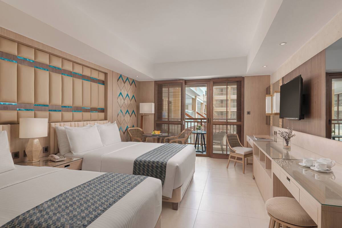 Ein Hotelzimmer mit zwei Betten, einem Schreibtisch, einem Fernseher und einem Balkon mit Holzjalousien.