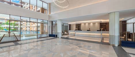 A spacious lobby with a reception desk, large windows, and a decorative ceiling light.