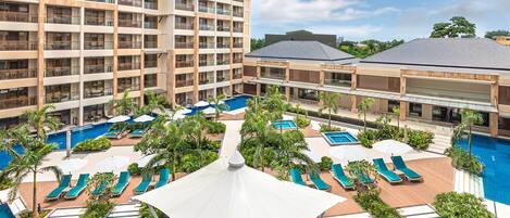 A hotel with multiple swimming pools, sun loungers, and a large building with balconies.
