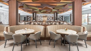 A modern restaurant with round tables and cushioned seating, featuring a geometric ceiling design and large windows. - Henann Tawala Resort (Panglao)