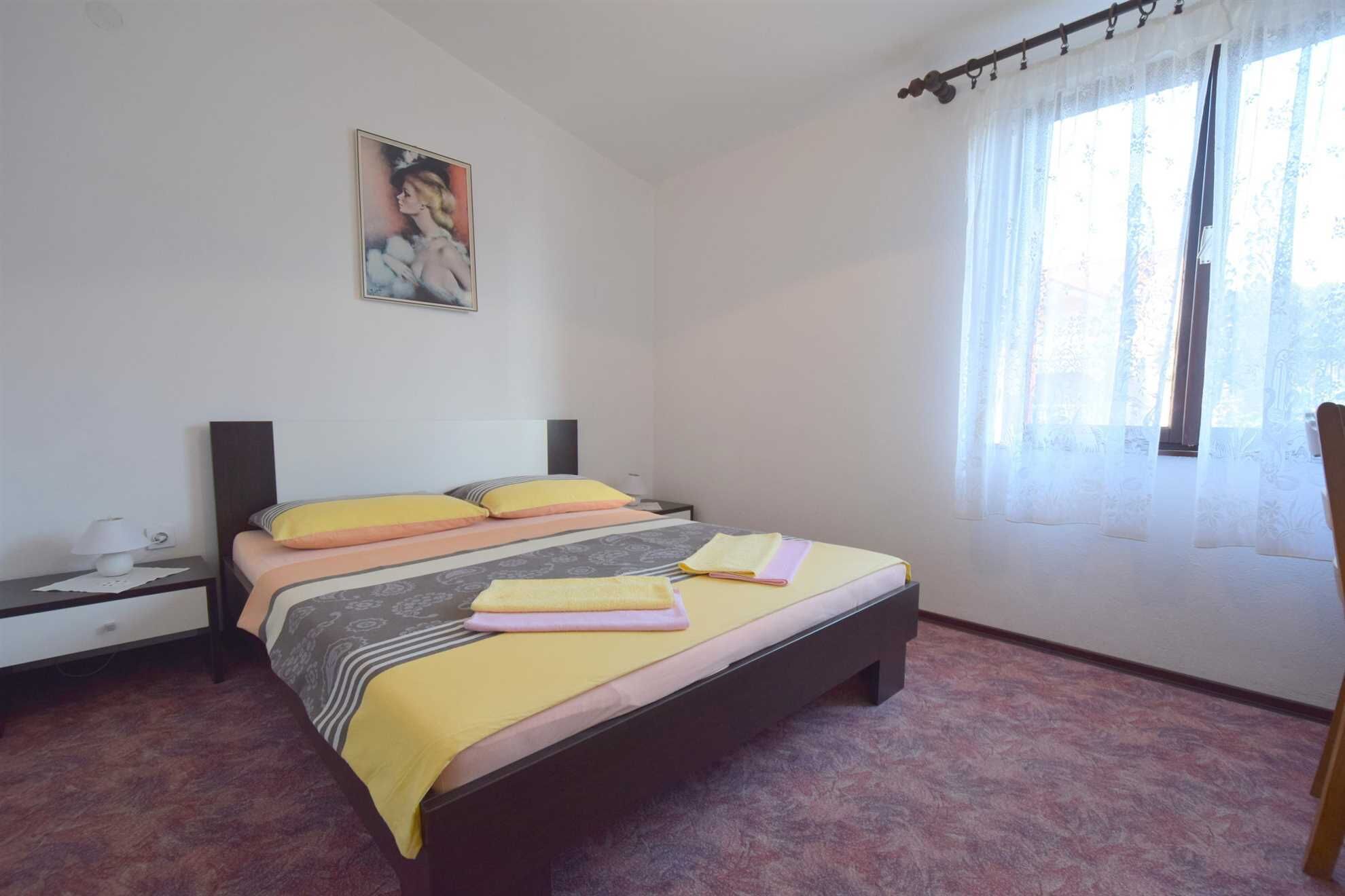 Ein Schlafzimmer mit einem Bett, einem Nachttisch, einer Lampe, einem Gemälde und einem Fenster mit Vorhängen.