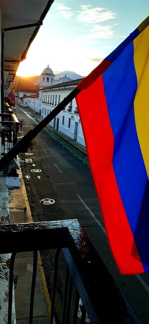 Una bandera en una barandilla con vista a una calle con edificios y un atardecer de fondo.