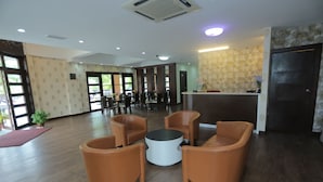 Een ruime lobby met een receptiebalie, een zithoek met stoelen en een groot raam dat voor natuurlijk licht zorgt.