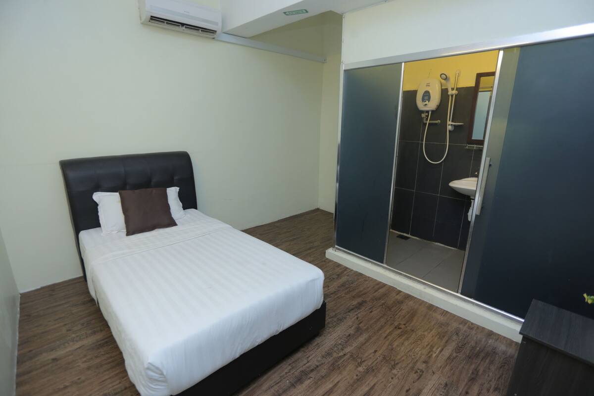 Een slaapkamer met een bed, een houten vloer en een schuifdeur naar een badkamer met douche en toilet.