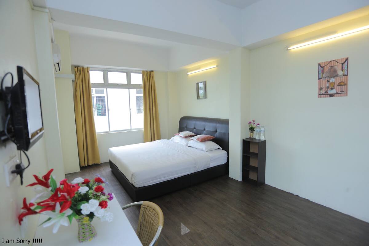 Een hotelkamer met een bed, een bureau met stoel, een kleine tafel met bloevas en een aan de muur bevestigde televisie.