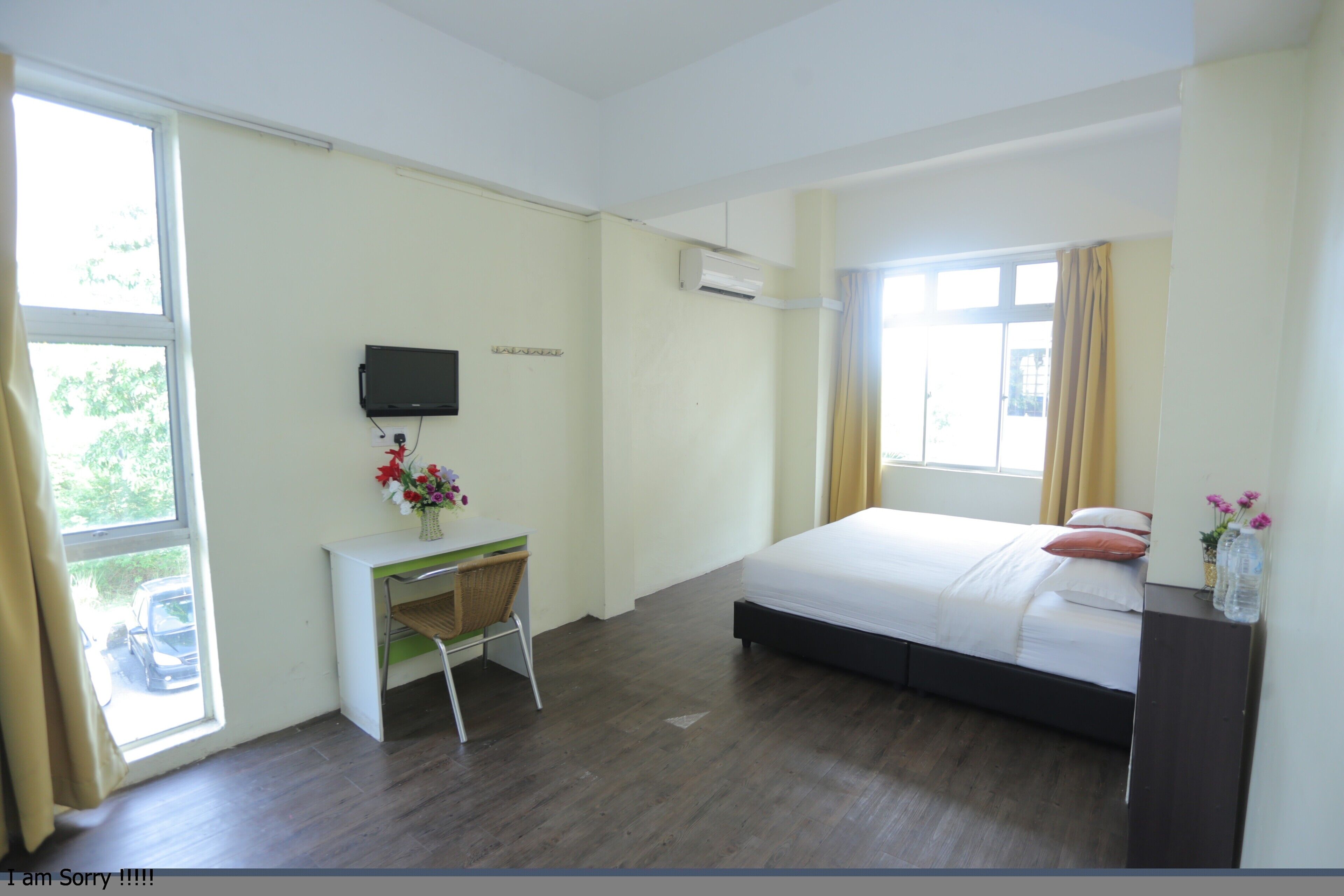A bedroom with a bed, a desk, a chair, a TV, and a window.