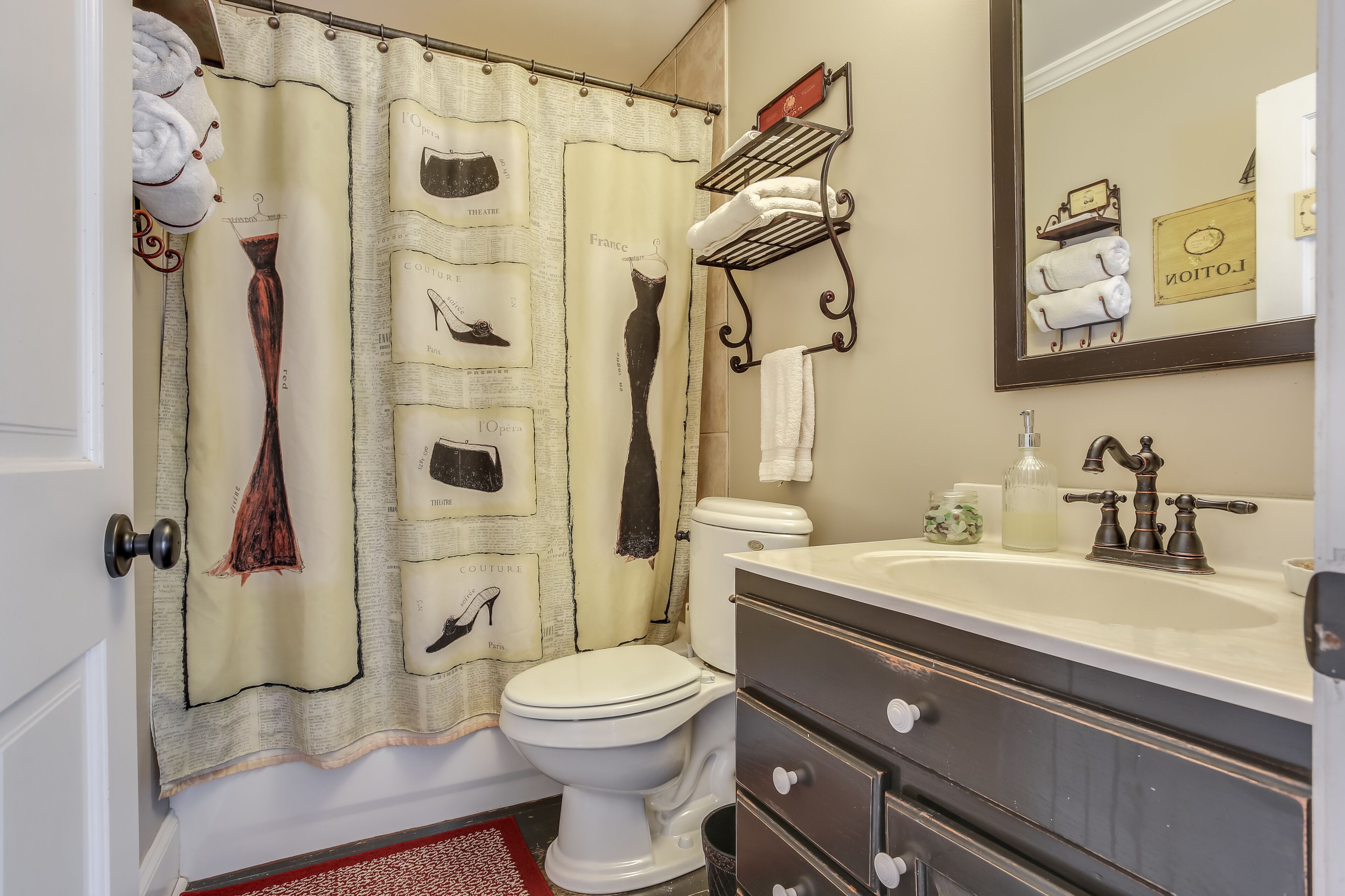 Une salle de bain avec un rideau de douche au motif rétro, des toilettes, un lavabo avec un miroir et un porte-serviettes avec des serviettes.