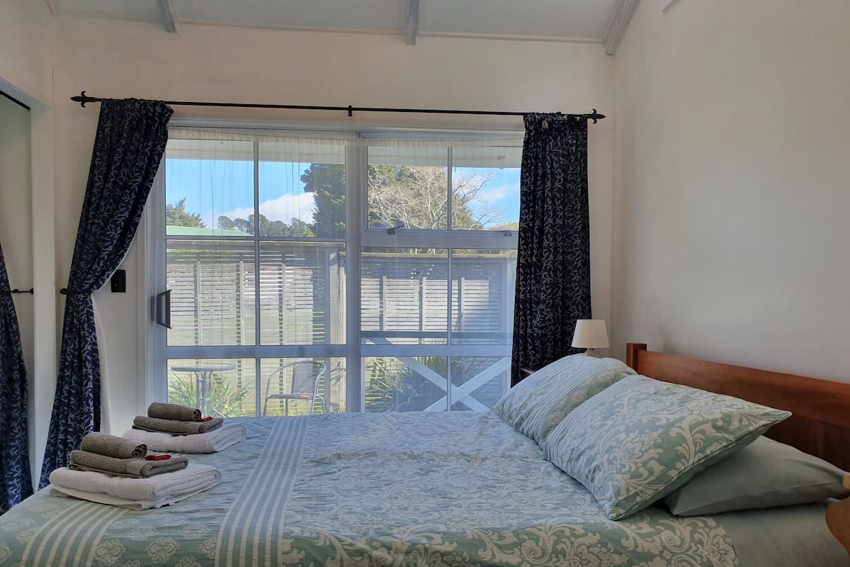 A bedroom with a bed, a nightstand, a window with curtains, and a view of the outside.