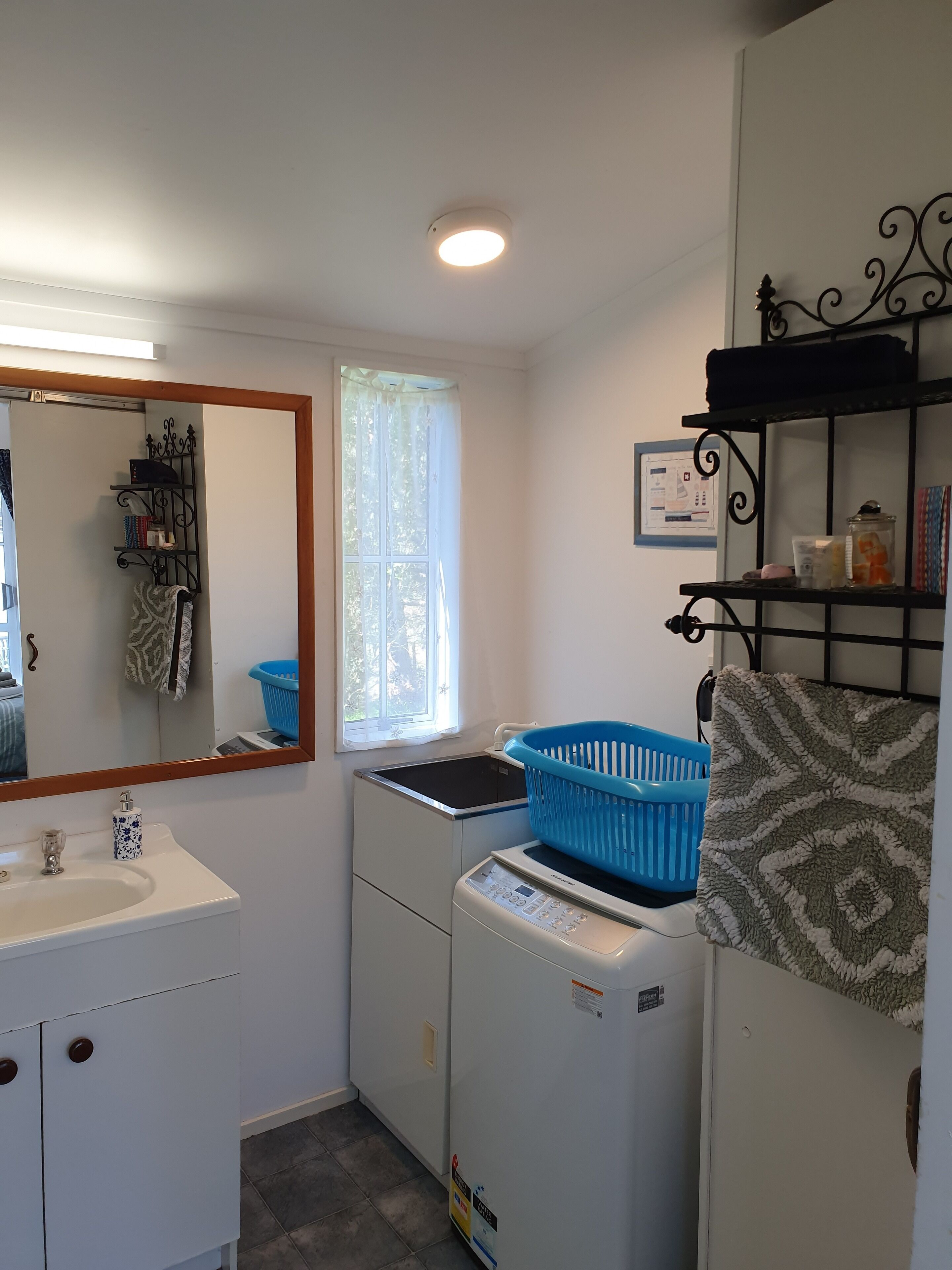 A compact bathroom with a sink, mirror, laundry machine, and a window with curtains.