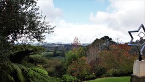 A landscaped garden with a prominent sculpture, a grassy area, and a view of distant hills. - Poripori Homestead (Lower Kaimai)